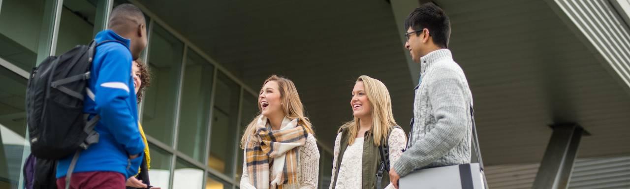 Diverse group of students standing outside in the fall laughing together.